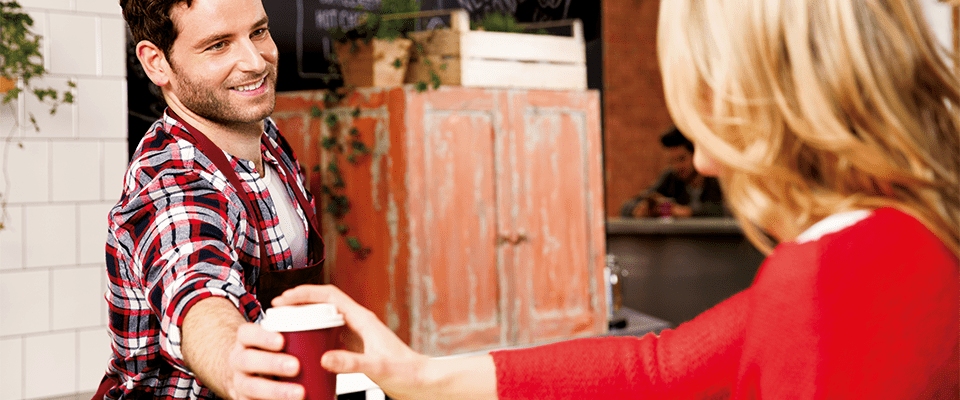 lucrător de cafenea în șorț roșu zâmbind în timp ce toarnă cafea pentru client