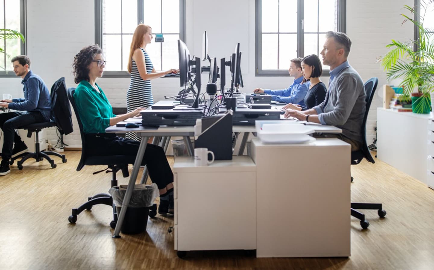 Сучасне офісне приміщення з п'ятьма людьми, які працюють за столами, за комп'ютерами, в оточенні великих вікон